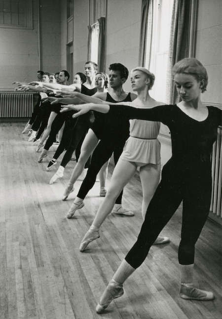Black and white photo of dancers at a ballet bar. 